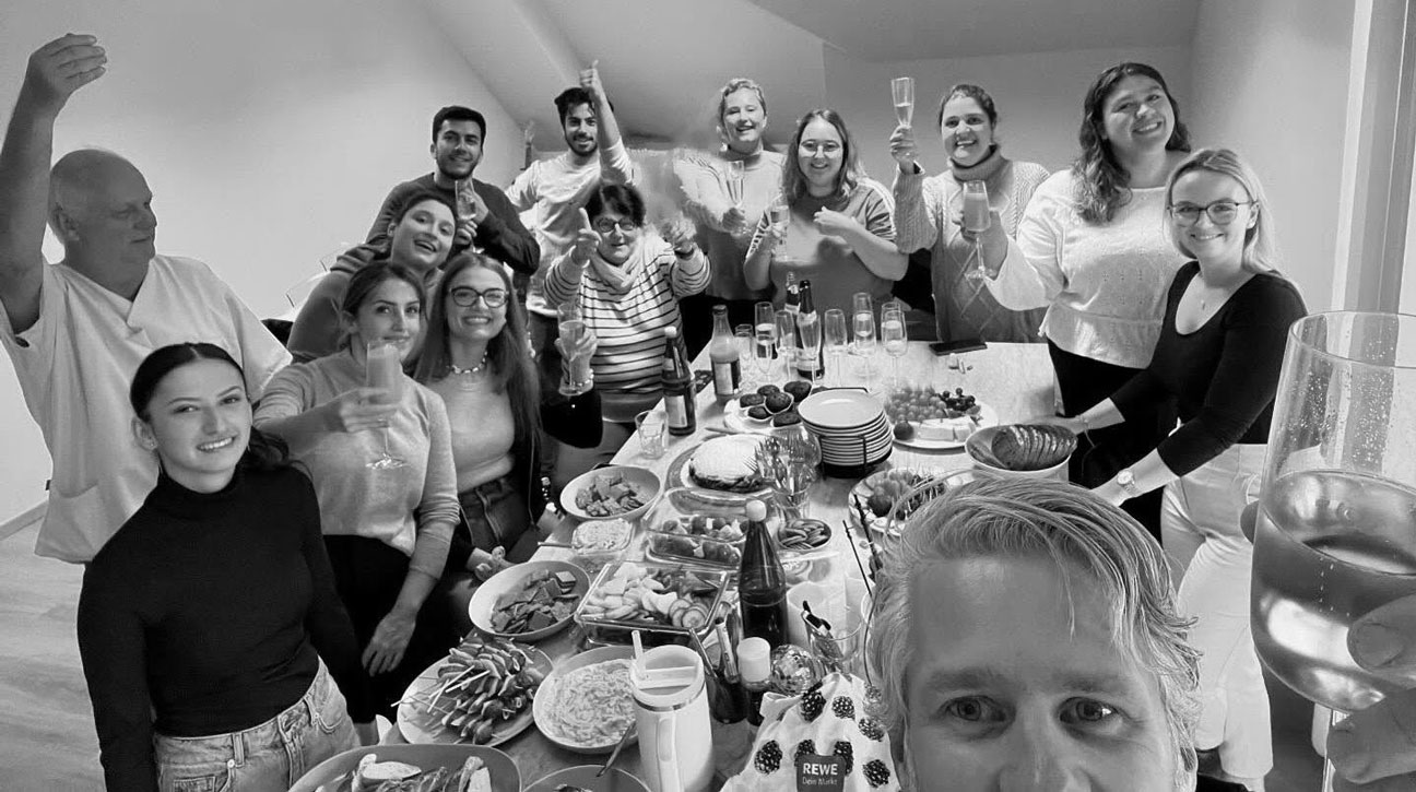 Foto des Teams bei einem Umtrunk. Personen heben das Glas und schauen in die Kamera.